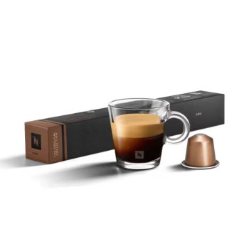 Clear glass espresso cup with crema, a copper coffee capsule, and a long black packaging box in the background.