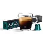 Glass cup of black coffee with crema, flanked by teal patterned coffee box and a teal capsule.